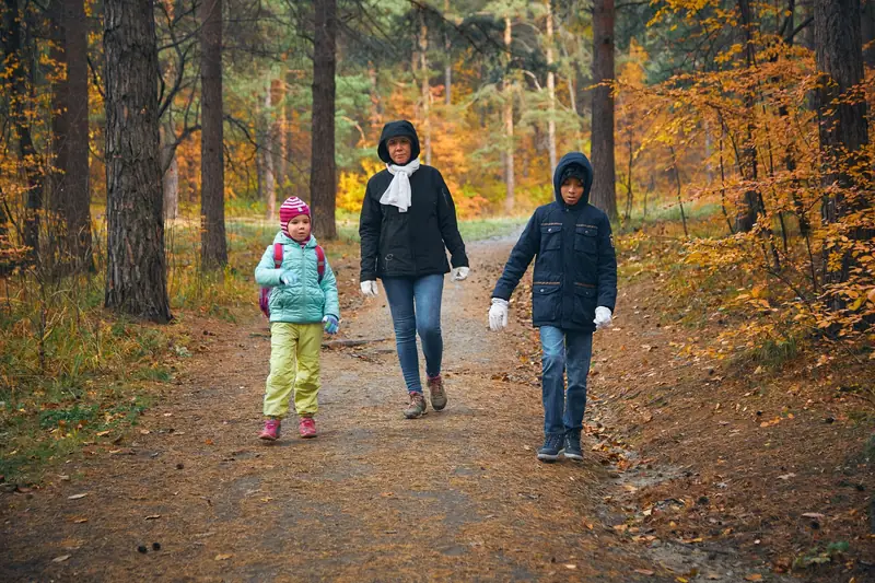 A mother walking with two children through an autumn forest