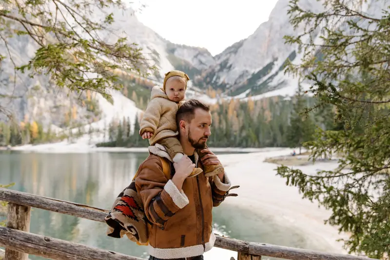 A father carrying his child on his shoulders beside a mountain lake