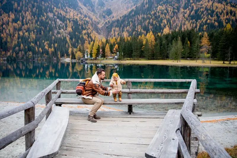 A father and child sitting on a wooden jetty at a mountain lake in autumn