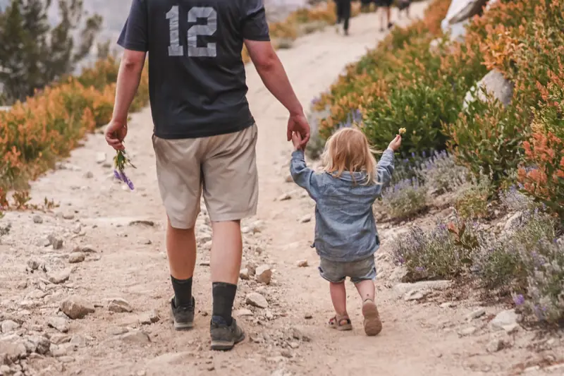 A father holding hands with a small girl on a rocky hiking trail