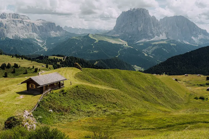 A small wooden hut on a grassy slope with mountains behind