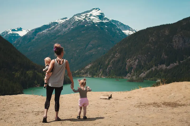 A mother walking with two small children above a turquoise mountain lake
