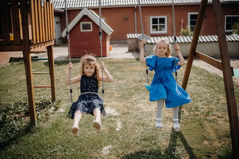 Two little girls on swings at a wooden playground